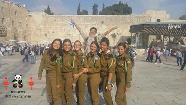תייר סיני בכותל המערבי הקופץ מהתלהבות מאחורי חיילות